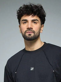Man wearing a black t-shirt and blue pants against a gray background